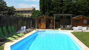 A rectangular swimming pool with a tiled edge, surrounded by green lawn and a wooden deck. - Les Lauriers Roses (Bollène)