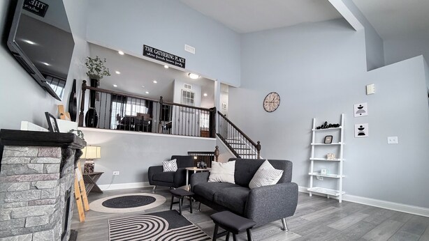 A modern living room with a fireplace, grey sofas, a staircase, and a bookshelf. - Modern Spacious Retreat with Fast Wi-Fi, Yard & Workspace - 4BR and 2 Full Bath (Waukegan)