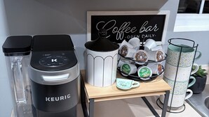 A coffee station with a Keurig coffee maker, a coffee grinder, and a mug rack with coffee pods. - Modern Spacious Retreat with Fast Wi-Fi, Yard & Workspace - 4BR and 2 Full Bath (Waukegan)