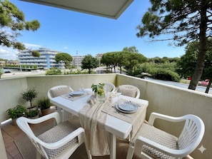 A balcony with a table set for two, surrounded by white chairs with patterned cushions, potted plants, and a clear view of the surrounding area. - Spacious Beachside Flat With Terrace (Caorle)