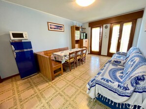 A compact living space with a dining table, a sofa, a refrigerator, and a television. - Spacious Beachside Flat With Terrace (Caorle)