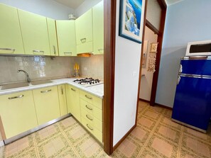A kitchen with light green cabinets, a gas stove, a sink, and a blue refrigerator. - Spacious Beachside Flat With Terrace (Caorle)