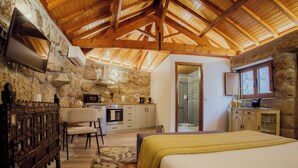 A bedroom with a bed, a desk, a chair, and a stone wall. - Refuge of Plenitude (Canelas)