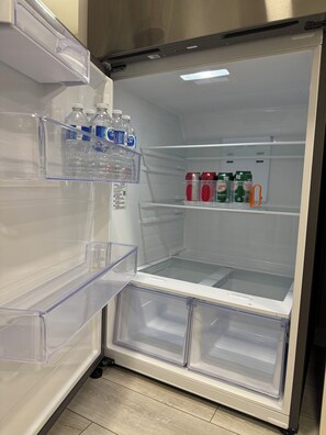 Ein offener Kühlschrank mit übersichtlichen Regalen, der Wasserflaschen und Dosen Canada Dry Ginger Ale enthält.