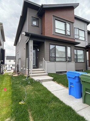 A modern two-story residential building with a visible front door, a small front yard, and a visible number '375' on the door.