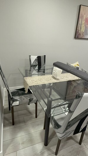 A dining area with a glass table and chairs, a lace table runner, and a painting on the wall.