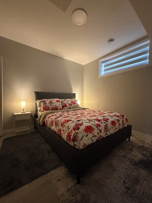 A bedroom with a bed, a nightstand, a window with blinds, and a ceiling light.