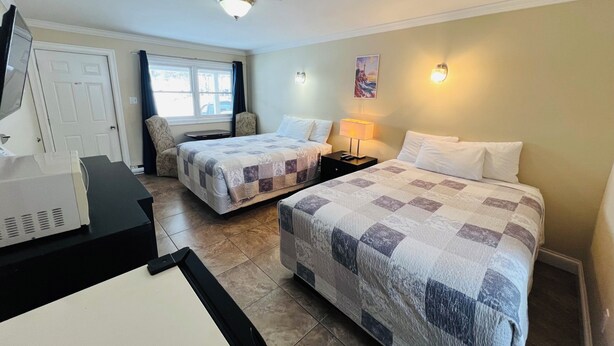 A hotel room with two beds, a desk, a chair, a lamp, and a painting on the wall.
