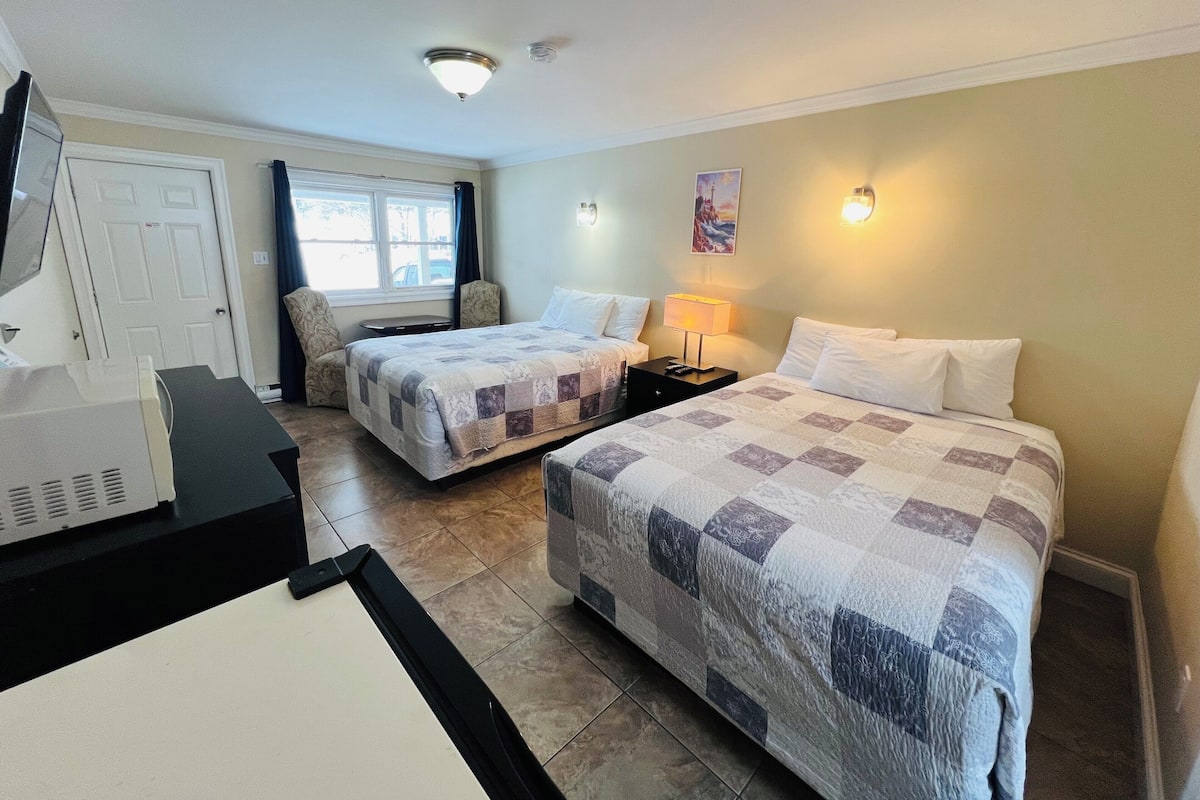 A hotel room with two beds, a desk, a chair, a lamp, and a painting on the wall.