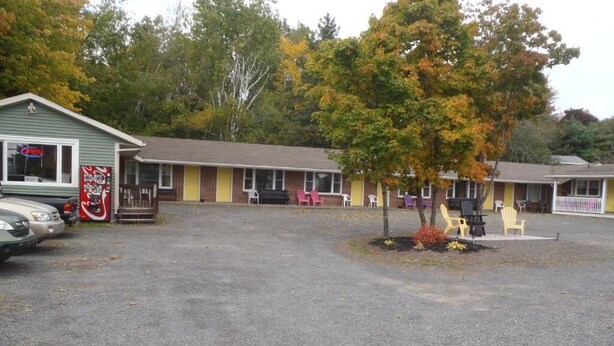 A motel with a gravel parking area, a small tree, and a row of motel rooms with chairs outside.