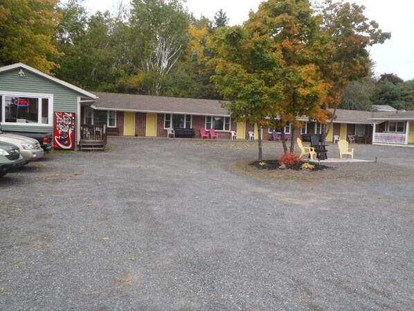 A motel with a gravel parking area, a small tree, and a row of motel rooms with chairs outside.