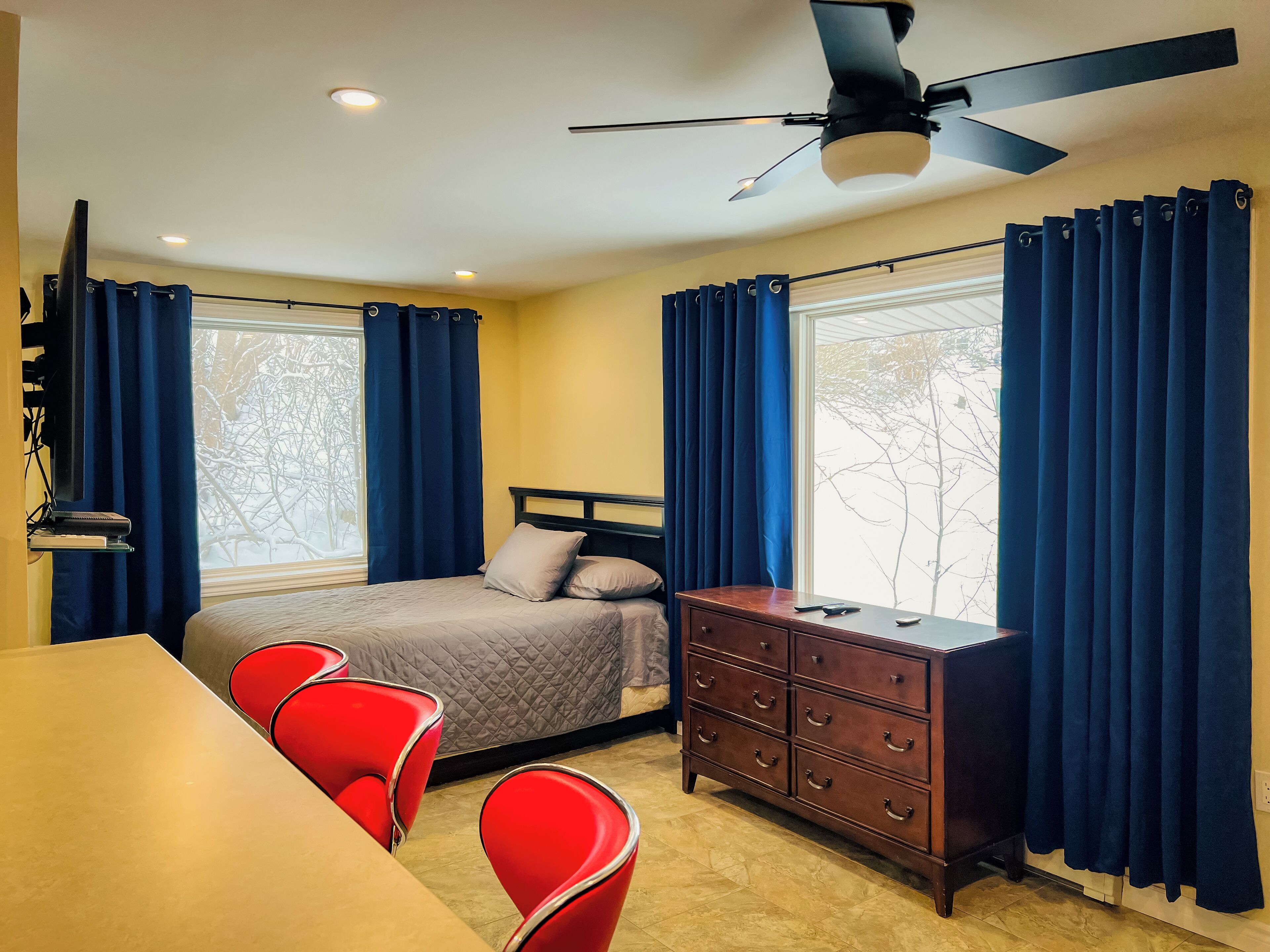 A hotel room with a bed, a desk, a dresser, and a ceiling fan.