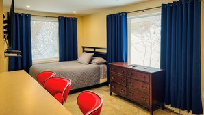 A hotel room with a bed, a desk, a dresser, and a ceiling fan.