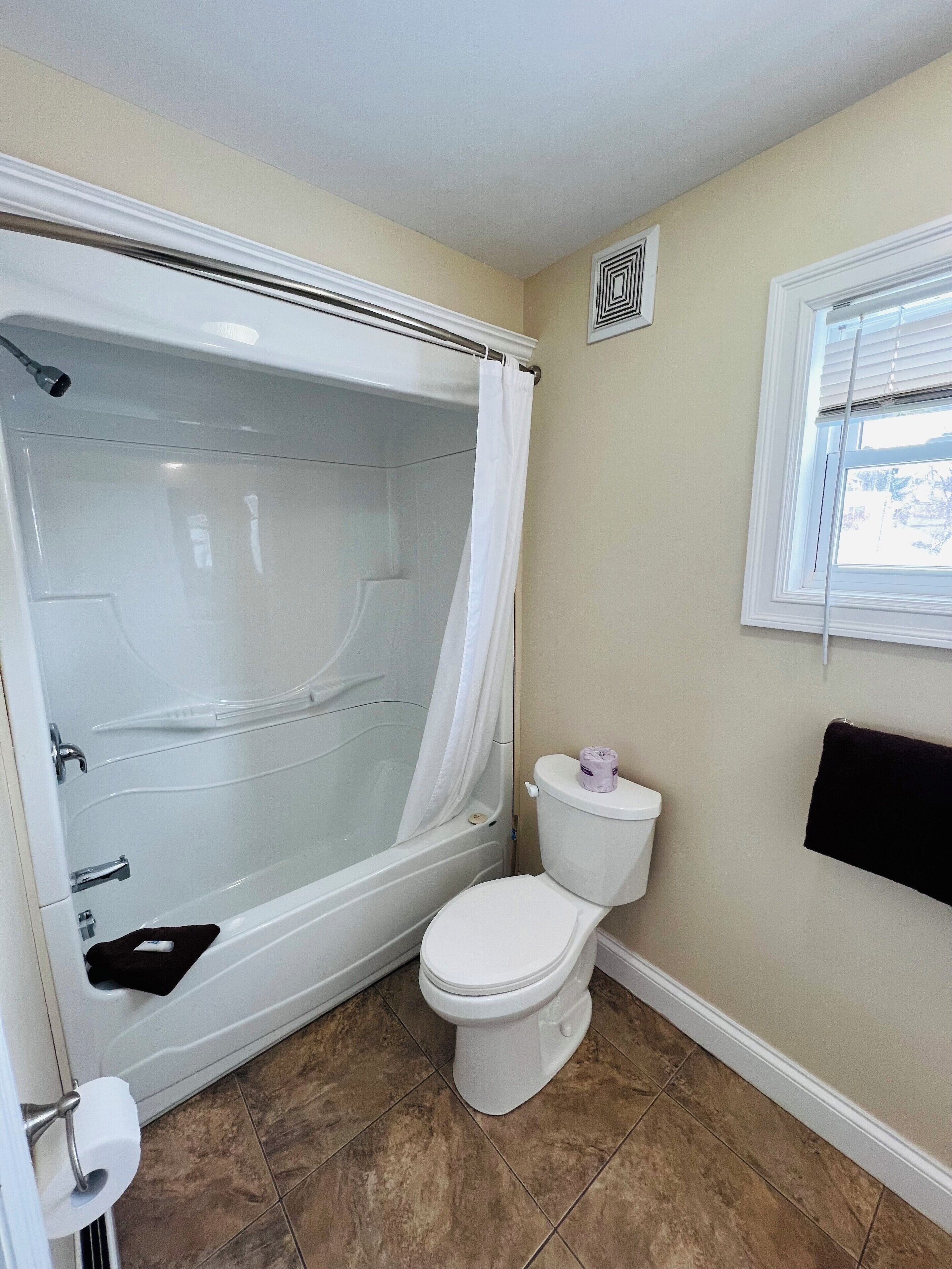 A bathroom with a bathtub, toilet, and a window.