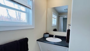 A bathroom with a window, a sink, a mirror, and a towel rack.