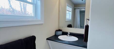 Un baño con ventana, lavabo, espejo y toallero.