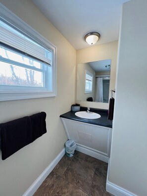 A bathroom with a window, a sink, a mirror, and a towel rack.