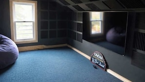 Quarto com uma janela grande, televisão de tela plana, um puff e um aviso na parede.