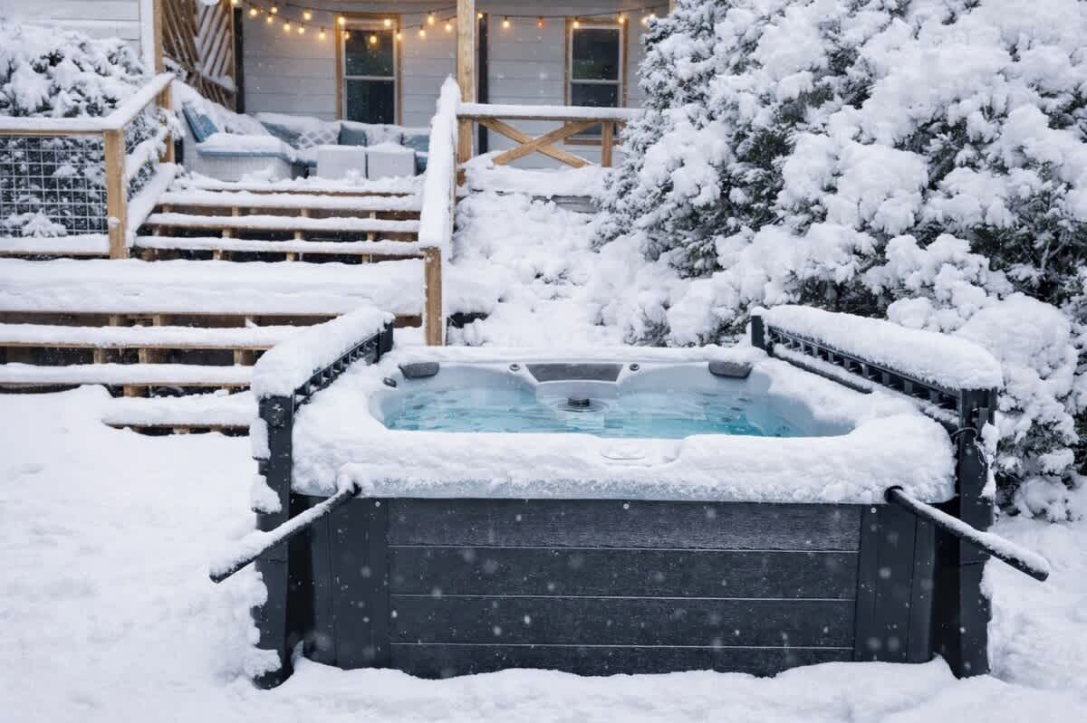 Un bain à remous entouré de marches recouvertes de neige et d’une terrasse en bois.