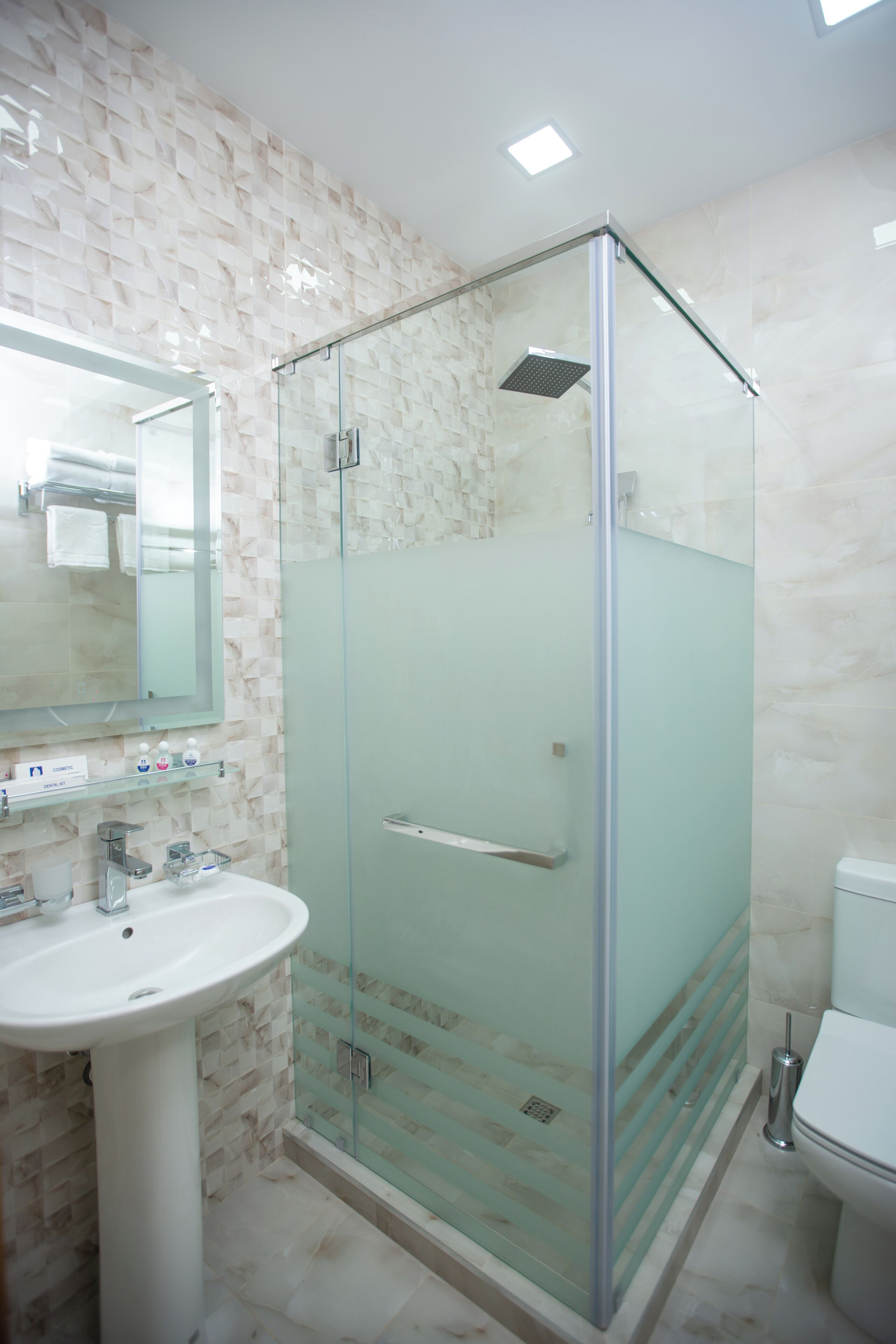 Un baño moderno con ducha acristalada, lavamanos blanco y un inodoro.