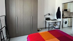 Een slaapkamer met een bed, een bureau met een laptop, een wasmachine en een kledingkast.