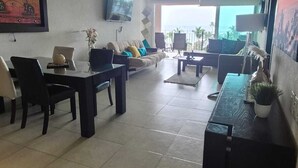 Ein geräumiger Wohnbereich mit einer Couch, Sesseln, einem Couchtisch und einem an der Wand befestigten Fernseher.