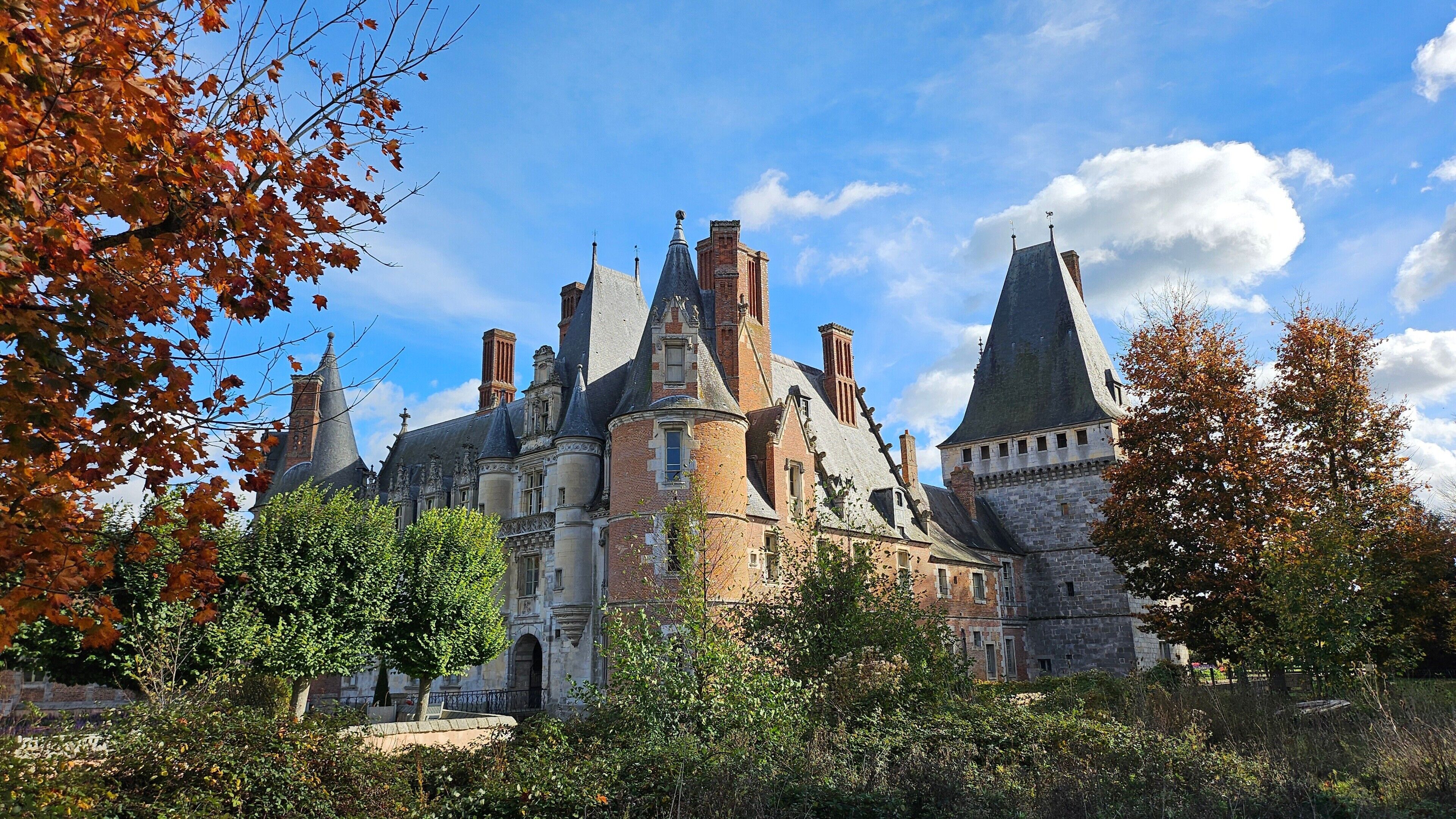 A historic building with multiple towers and turrets, surrounded by trees and greenery.