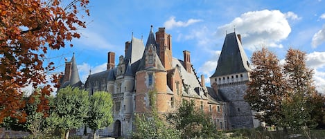 A historic building with multiple towers and turrets, surrounded by trees and greenery.