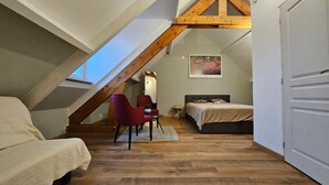 Ein Schlafzimmer im Loft-Stil mit schrägverdeckter Decke, einem Bett, einem roten Sessel, einem kleinen Tisch und einem Bild an der Wand.