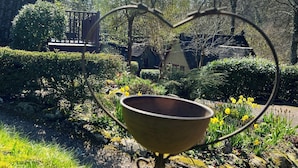 Un jardin agrémenté d’une structure métallique en forme de cœur et d’un récipient métallique.