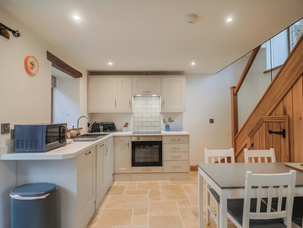 A compact kitchen with white cabinets, a microwave, a sink, and a dining area with a table and chairs. - Rose Cottage (Wellington)