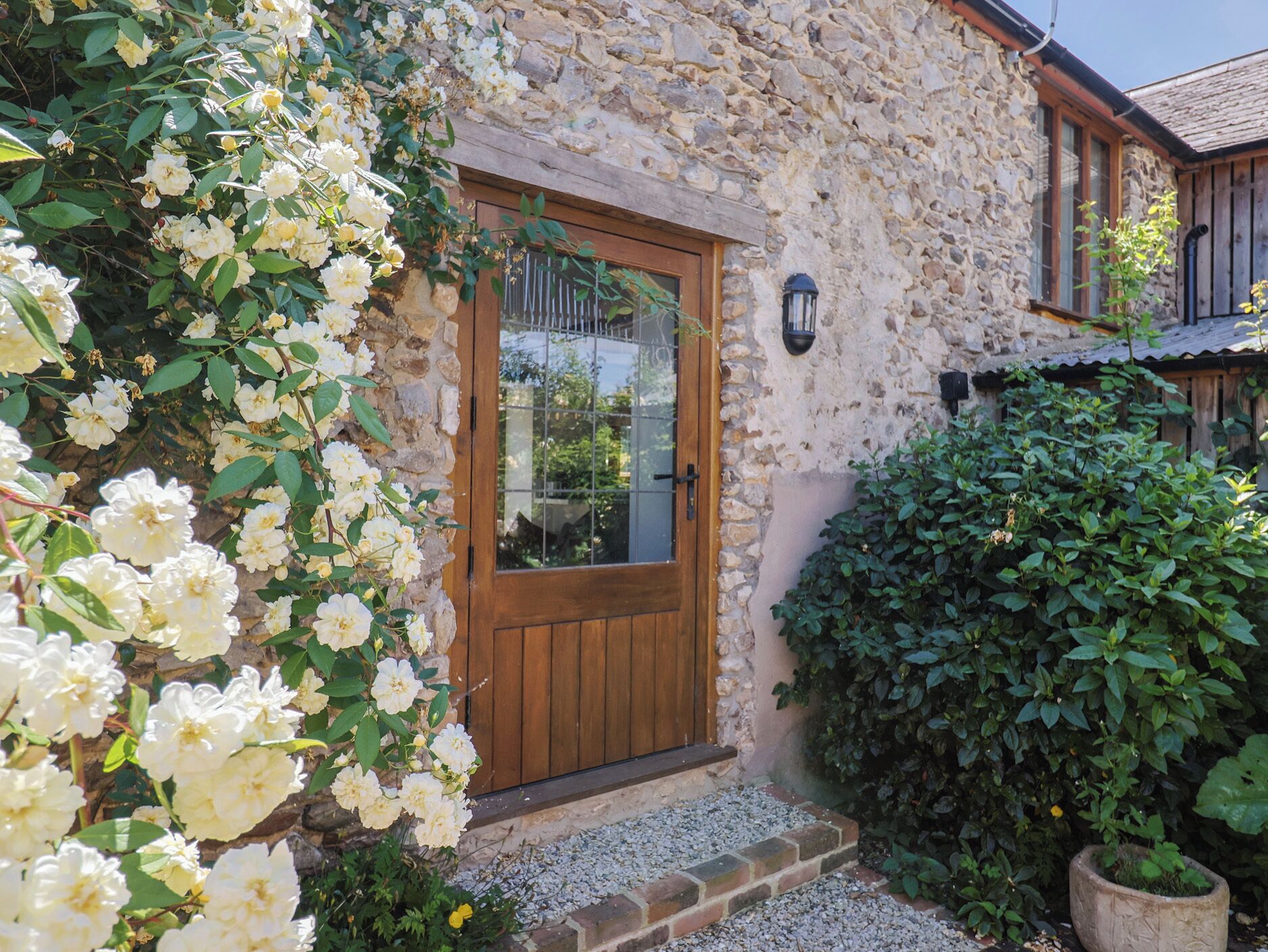 A stone building with a wooden door, a gravel pathway, and a large bush.