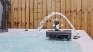 A hot tub with water flowing into two glasses, set against a wooden fence backdrop. - Rose Cottage (Wellington)