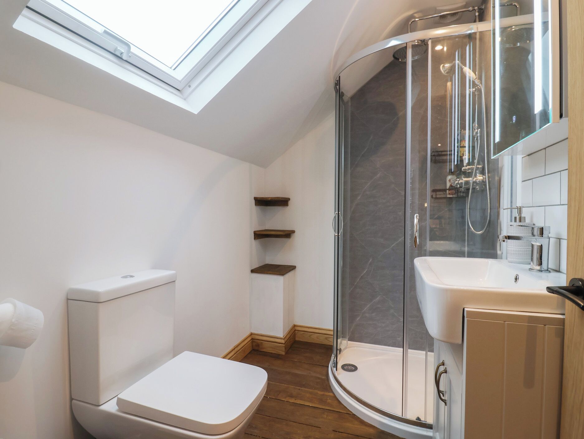 A modern bathroom with a skylight, a glass-enclosed shower, a toilet, and a sink.