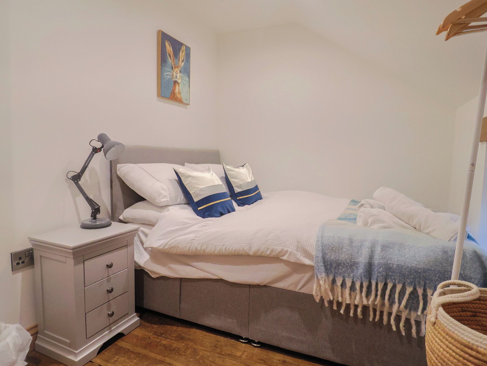 A neatly made bed with white and blue bedding, a bedside lamp, and a small bedside table with drawers.