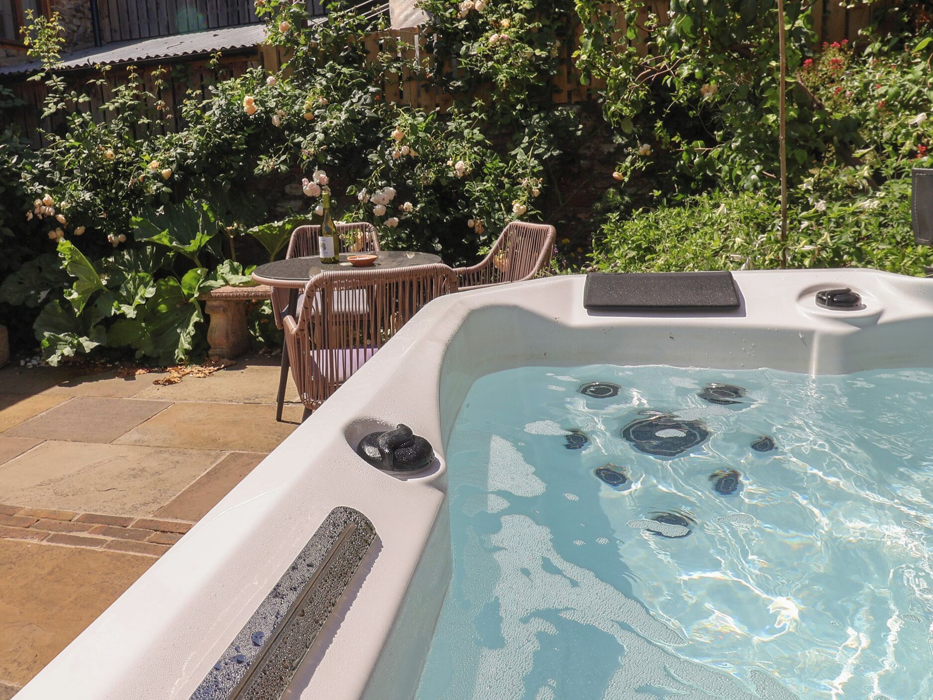 A hot tub with jets, surrounded by a garden with roses and a wooden fence.