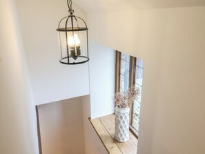 A modern interior with a hanging lantern, a white vase with dried flowers, and a window with a view. - Rose Cottage (Wellington)