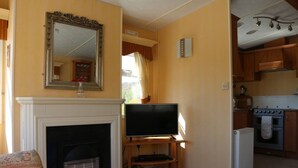 A living room with a fireplace, a television, and a kitchen area visible through an open doorway.