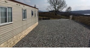 A single-story mobile home with a gravel driveway and a wooden fence.
