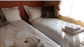 A hotel room with two beds, each with white linens and a rolled towel on top.
