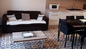 A compact living space with a sofa, a coffee table, a dining table with chairs, a microwave, and a sink in the kitchen area.