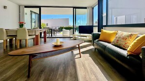 Een moderne woonkamer met een houten salontafel, een bank met gele kussens, en een televisie.