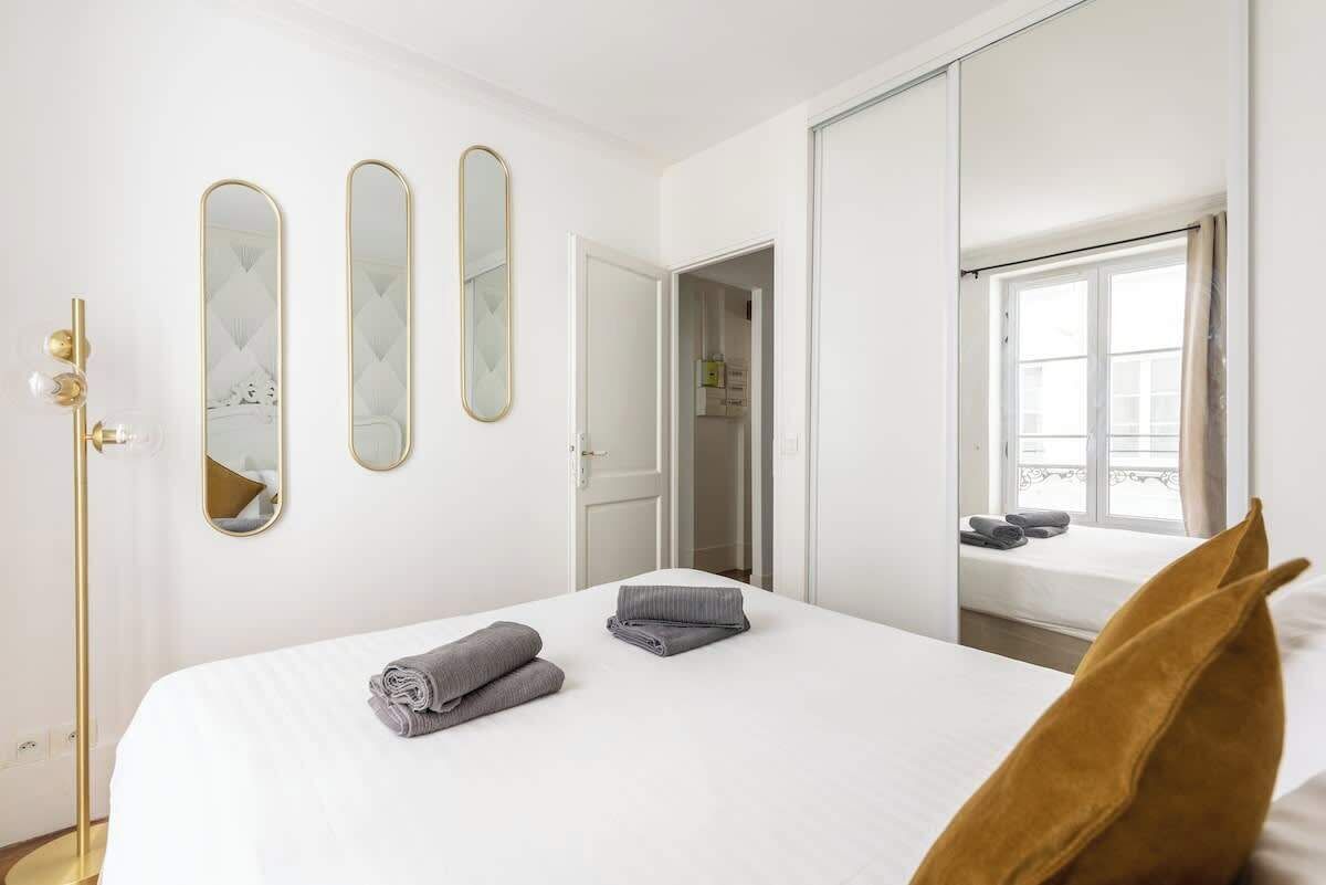 A hotel room with a bed, two mirrors, a wardrobe, and a window with a view.