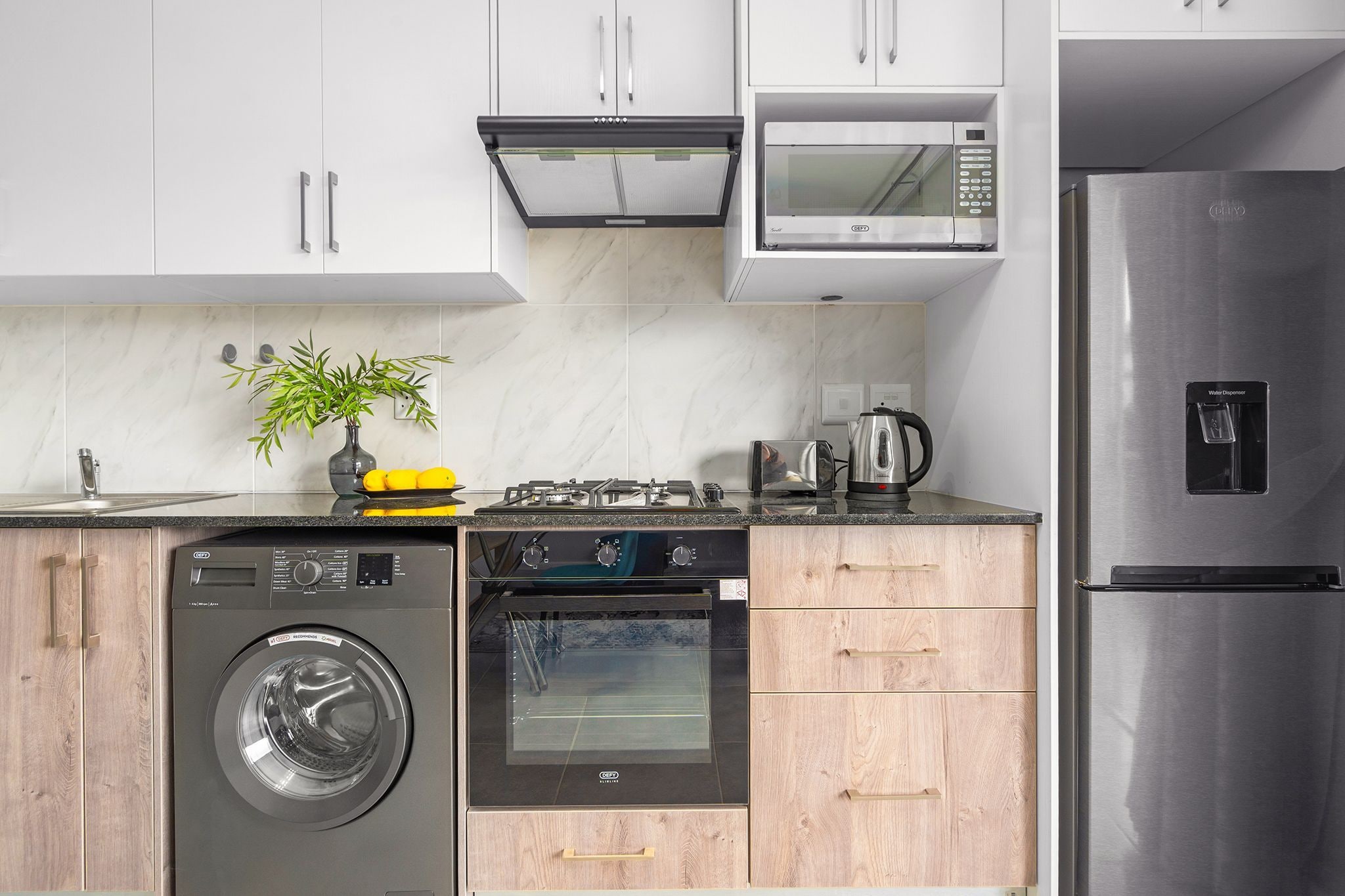 A modern kitchen with a stainless steel refrigerator, a built-in oven, a microwave, and a washing machine.