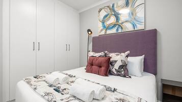 A bedroom with a large bed, a headboard, a wall art piece, and a floor lamp.
