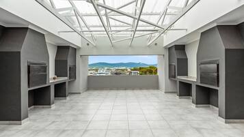 A spacious room with a high ceiling and skylight, featuring a large window with a view of distant buildings and mountains.