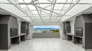 Une pièce spacieuse avec un plafond haut et un puits de lumière, dotée d’une grande fenêtre offrant une vue sur des bâtiments et des montagnes situés au loin.