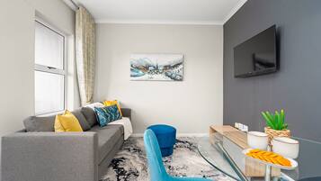 A modern living room with a grey sofa, blue armchair, and a glass coffee table.