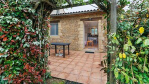A stone building with a tiled patio, a table, and a wooden pergola. - Cottage for 2 with Heated Pool and Wi-Fi in Quiet Sarlat Setting (Sarlat-la-Canéda)