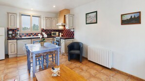 A kitchen with a dining table, chairs, a microwave, and a window. - Cottage for 2 with Heated Pool and Wi-Fi in Quiet Sarlat Setting (Sarlat-la-Canéda)